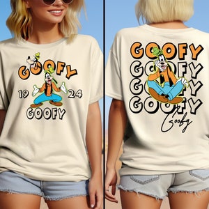 May include: A cream-colored t-shirt with a cartoon image of Goofy wearing a blue shirt and orange pants. The shirt has the text "GOOFY" in orange and black letters, with the numbers "19" and "24" on either side of the image. The back of the shirt has the text "GOOFY" repeated four times in orange and black letters, with a cartoon image of Goofy sitting down in the middle. The text "Goofy" is written in cursive at the bottom of the shirt.