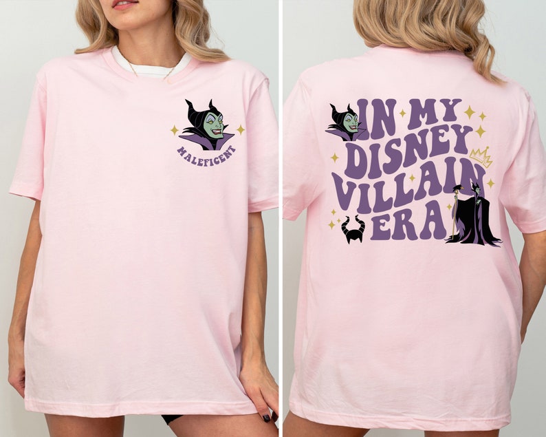 May include: Pink t-shirt featuring a purple and green image of Maleficent from Disney's Sleeping Beauty. The back of the shirt displays the text "In My Disney Villain Era" in purple with a gold crown and a purple and black image of Maleficent.