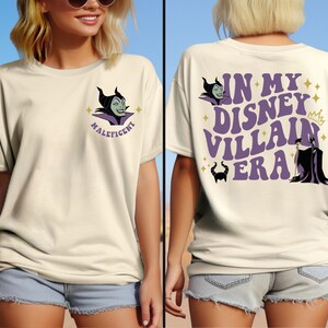 May include: A white t-shirt featuring a purple graphic of Maleficent from Disney's Sleeping Beauty. The graphic includes the text "Maleficent". The back of the shirt has a purple graphic that says "In My Disney Villain Era" with a crown and a silhouette of Maleficent.