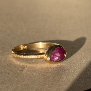 May include: A gold ring with a textured band and a deep red, faceted gemstone.