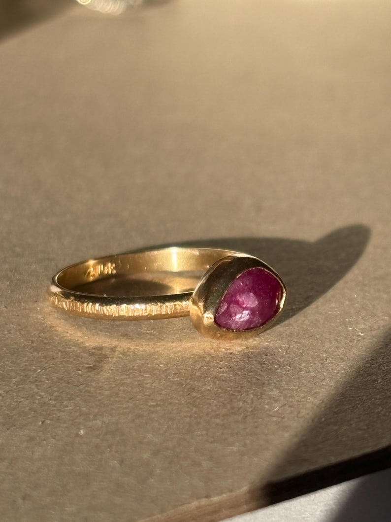 May include: A gold ring with a textured band and a deep red, faceted gemstone.