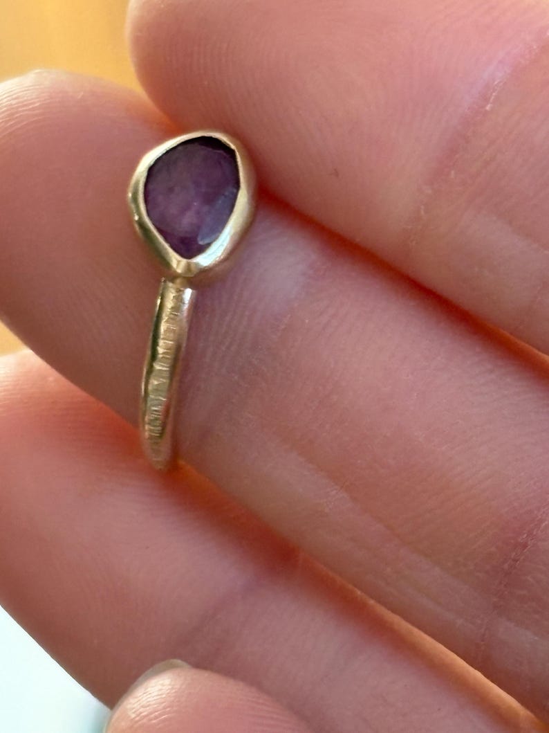 May include: A silver ring with a textured band and a purple gemstone set in a leaf-shaped setting.