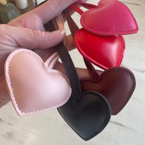 May include: Four heart-shaped leather keychains in different colors: pink, red, burgundy, and black. Each keychain has a stitched edge and a loop for attaching keys.