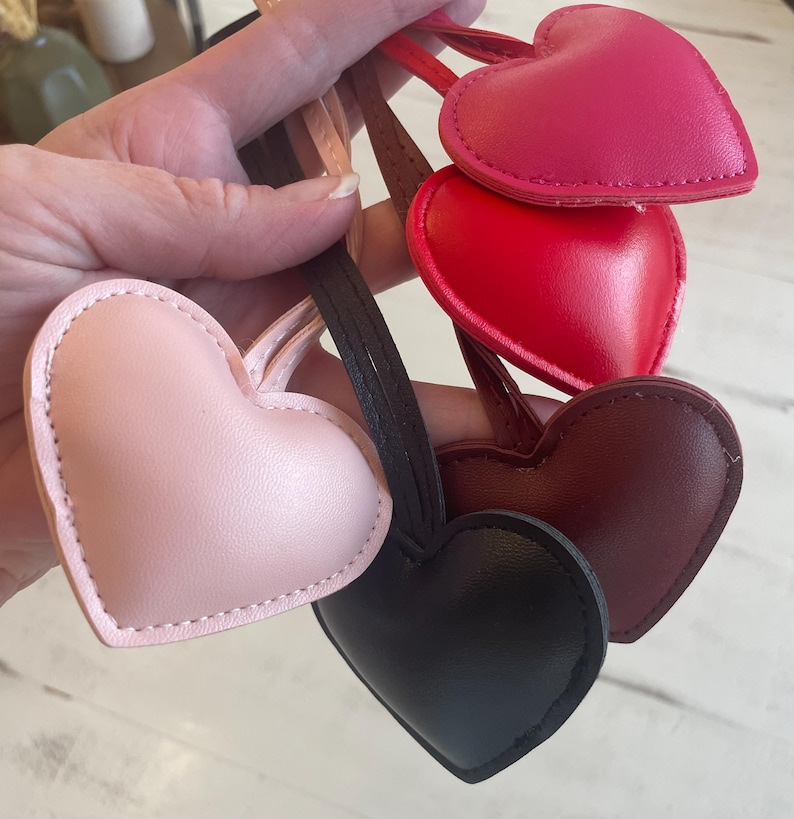 May include: Four heart-shaped leather keychains in different colors: pink, red, burgundy, and black. Each keychain has a stitched edge and a loop for attaching keys.