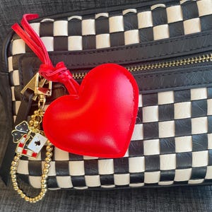 May include: A black and white checkered handbag with a red heart-shaped charm attached to a gold chain with a small playing card charm.