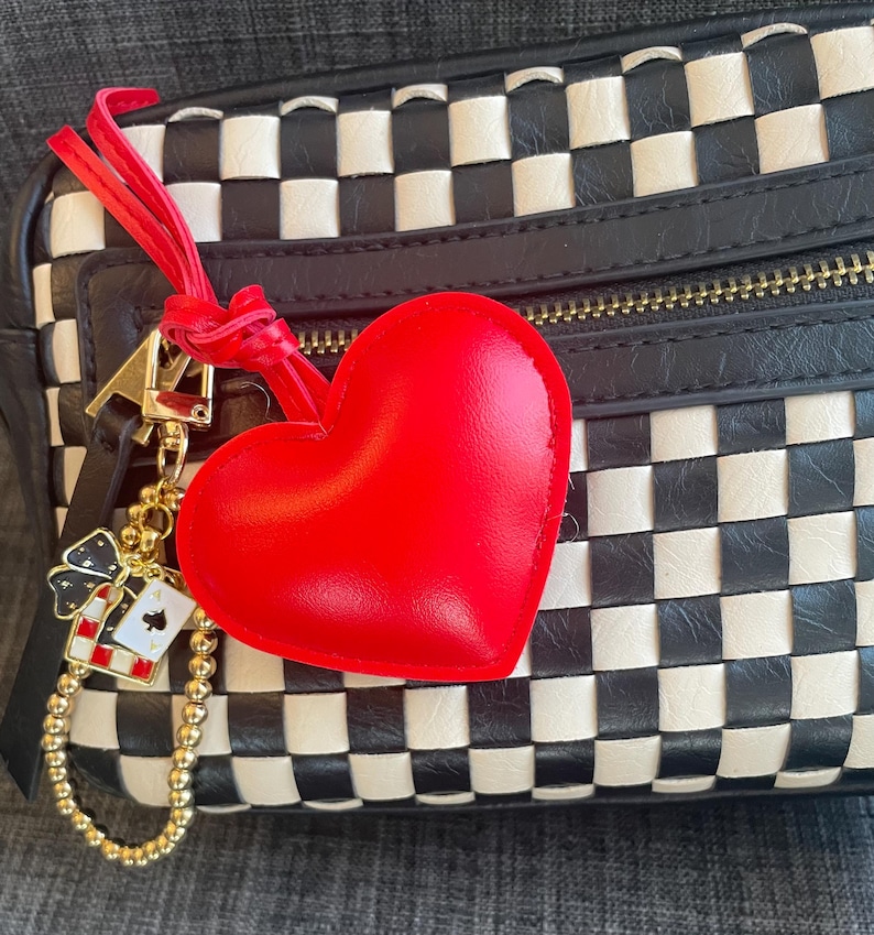 May include: A black and white checkered handbag with a red heart-shaped charm attached to a gold chain with a small playing card charm.