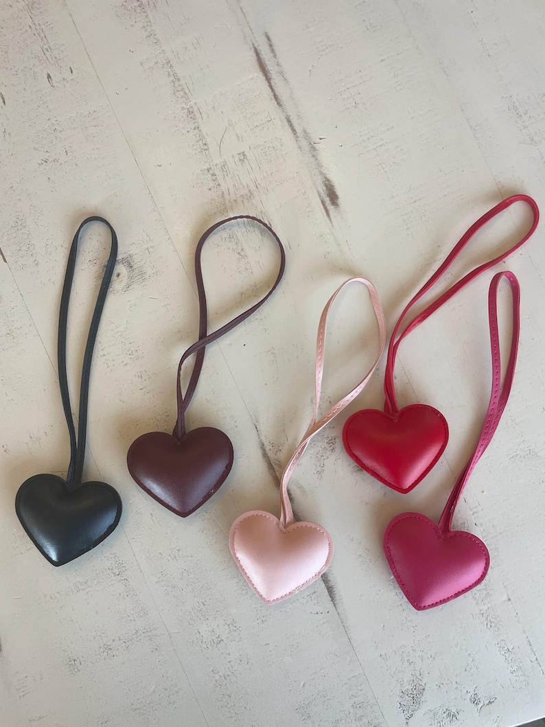 May include: Five leather heart-shaped keychains with different colored straps. The keychains are black, burgundy, pink, red, and a darker shade of pink.