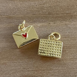 May include: Two gold-colored charms, one shaped like an envelope with a red heart, and the other with a textured surface.
