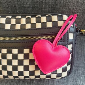 May include: A black and white checkered leather handbag with a pink heart-shaped charm attached to the zipper pull.