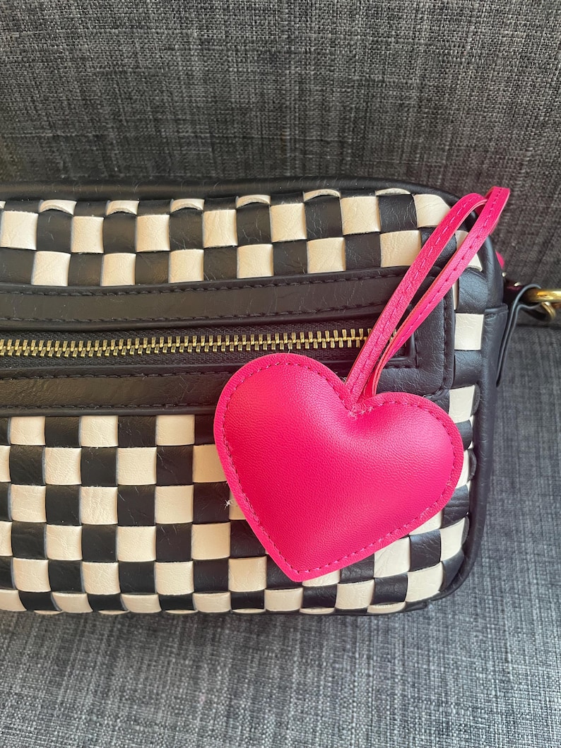 May include: A black and white checkered leather handbag with a pink heart-shaped charm attached to the zipper pull.
