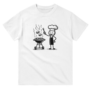 May include: A white t-shirt featuring a black and white illustration of a stick figure chef grilling burgers. The chef is wearing a hat and an apron. The chef is holding a spatula and there are three burgers on the grill.