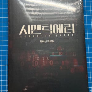 May include: A black book with the title "Semantic Error" in Korean and English. The subtitle is "Jayson Script" in Korean. The cover features a dark background with a digital pattern of binary code in red and green.