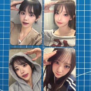 May include: Four photo cards showing a person posing. The person is wearing a gray hoodie, a light brown top, and a gray sweatshirt. The background is a blue grid. The cards are in a clear plastic sleeve.