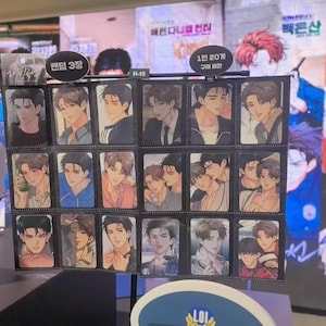 Peut inclure: Présentoir de cartes à collectionner avec des illustrations de style anime de personnages masculins. Les cartes sont disposées en rangées et en colonnes, chacune présentant un personnage différent dans diverses poses et tenues. Le présentoir comprend du texte coréen.