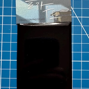 Puede incluir: Fotocard negra con acabado brillante. El anverso de la tarjeta presenta una ilustración colorida de una escena de clase con el texto "COLLECTION PHOTOCARD" y texto coreano.