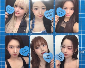 May include: Six trading cards featuring young women. Each card has a photo of a woman holding a blue heart-shaped sign with Korean text. The cards are in protective sleeves on a blue grid background.