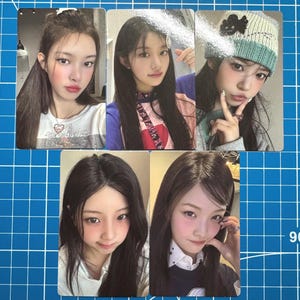 May include: Five photo cards featuring young women with long dark hair. The cards show the women in various poses, some with makeup and accessories. One woman wears a knit hat with a flower design. The background is a blue grid.