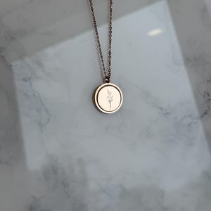May include: A gold chain necklace with a round pendant featuring a delicate floral design.