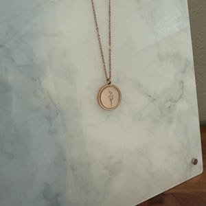 May include: A rose gold necklace with a delicate floral design pendant. The pendant is round and has a simple, minimalist style.