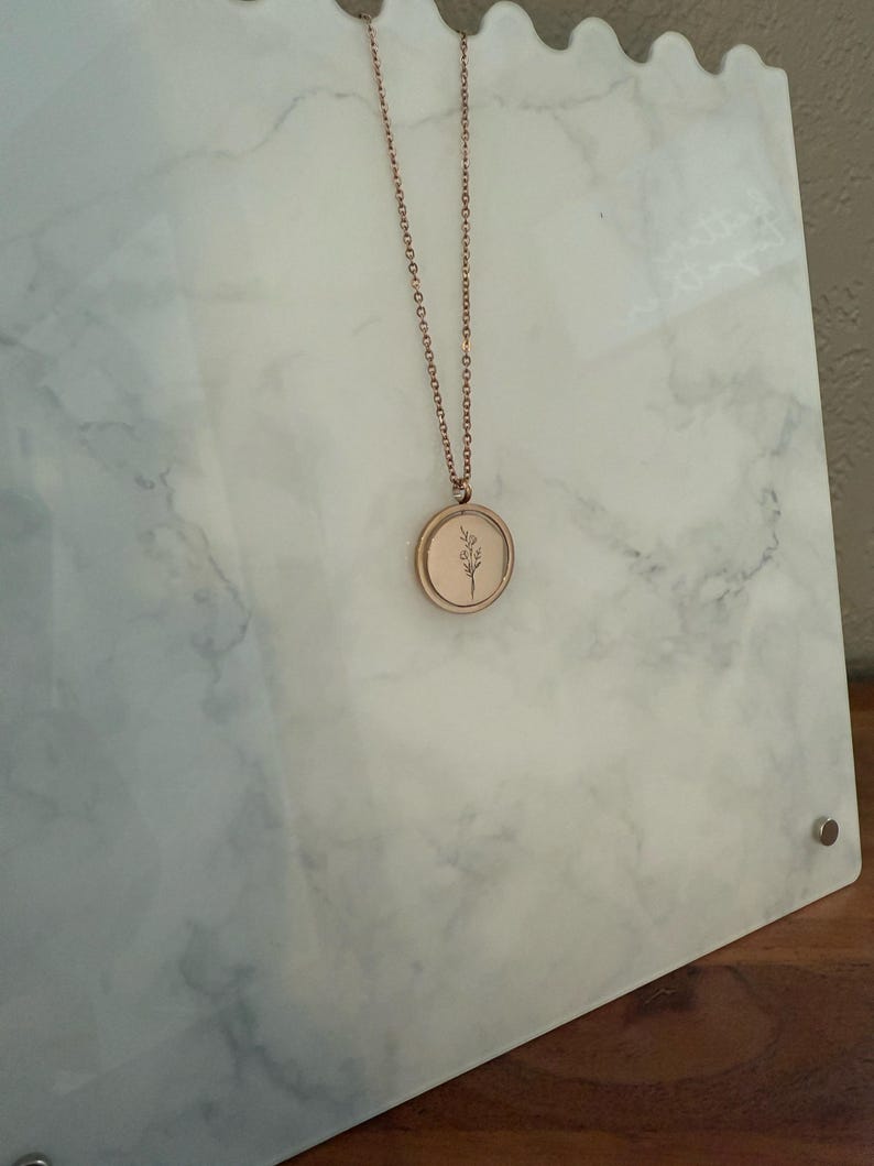 May include: A rose gold necklace with a delicate floral design pendant. The pendant is round and has a simple, minimalist style.