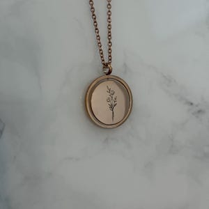May include: A rose gold necklace with a round pendant featuring a delicate floral design. The pendant is on a chain with a delicate link pattern.