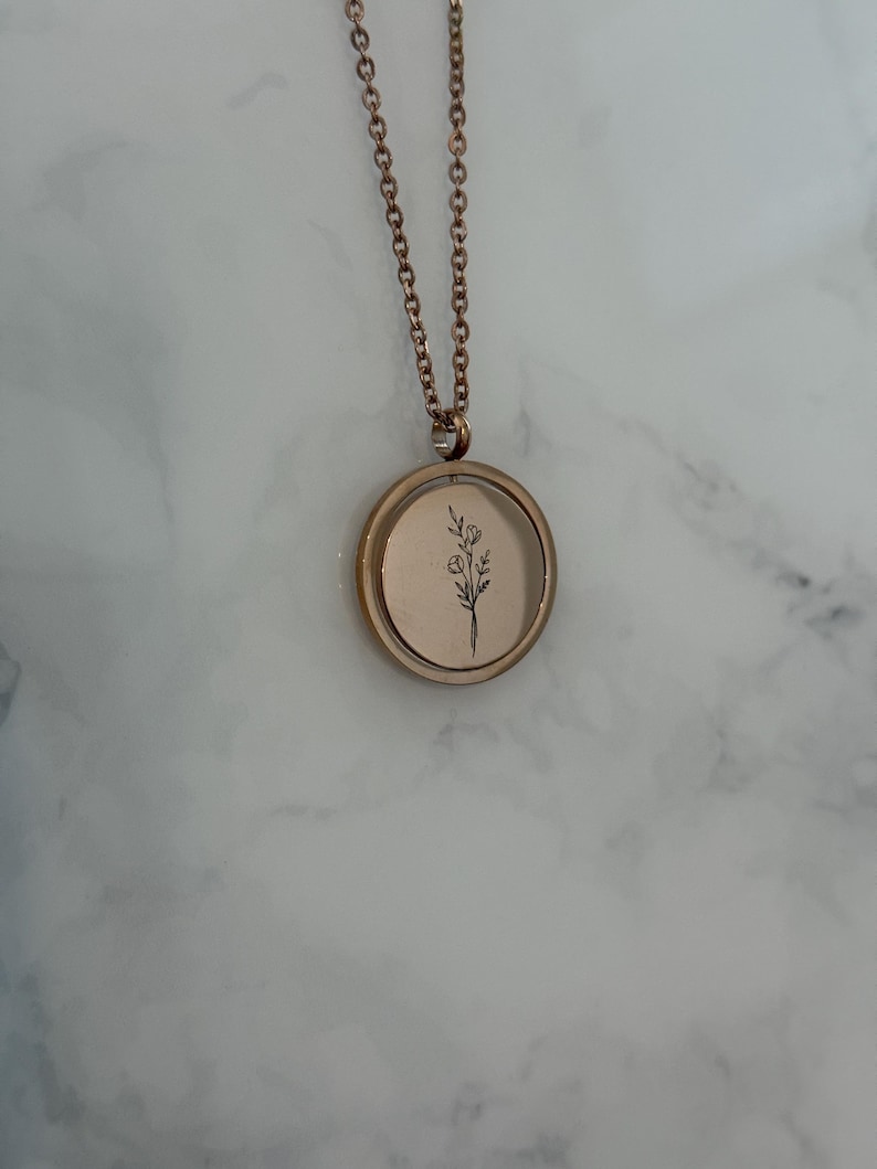 May include: A rose gold necklace with a round pendant featuring a delicate floral design. The pendant is on a chain with a delicate link pattern.