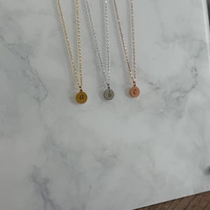 May include: Three gold, silver, and rose gold necklaces with small round pendants. Each pendant has a letter engraved on it: 'a', 'b', and 'c'.