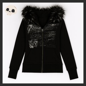 May include: Black zip-up hoodie with a faux fur-trimmed hood. The hoodie features a white graphic design on the front and a skull graphic in the upper left corner. The hoodie has a full zipper and two front pockets.