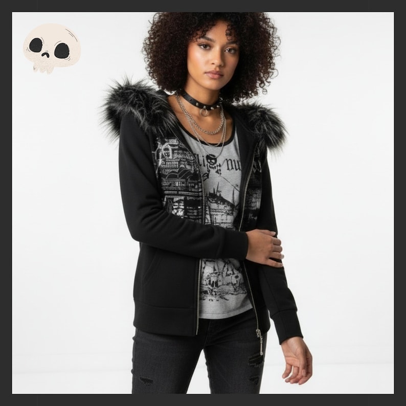 May include: Black zip-up hoodie with faux fur trim on the hood. The hoodie features a graphic print on the front and is worn over a gray graphic tee. The model is also wearing black jeans and multiple necklaces.