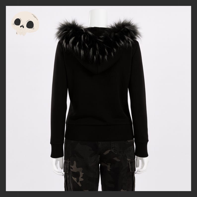 May include: A black hooded sweatshirt with a faux fur trim around the hood. The sweatshirt is displayed on a mannequin. The model is wearing camouflage cargo pants. A cartoon skull is in the upper left corner.
