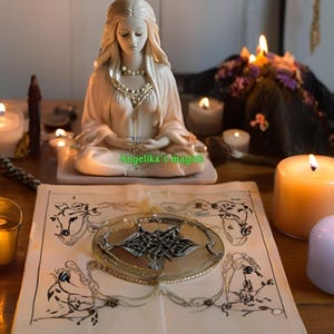 Pu&ograve; includere: Una statuetta di ceramica bianca di una donna seduta in una posa meditativa con le mani in grembo. La statuetta &egrave; circondata da candele accese, un libro e altri oggetti associati alla stregoneria. Il testo "Angelika's Magick" &egrave; visibile sul libro.