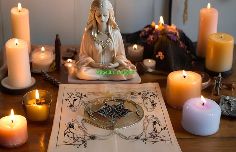 Pu&ograve; includere: Una statuetta di ceramica bianca di una donna seduta in una posa meditativa con le mani in grembo. La statuetta &egrave; circondata da candele accese, un libro e altri oggetti associati alla stregoneria. Il testo "Angelika's Magick" &egrave; visibile sul libro.