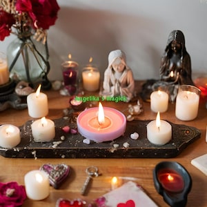 Pu&ograve; includere: Un tavolo con una variet&agrave; di candele bianche, una candela rosa e un portacandele rosa. Ci sono anche fiori, un libro e altri oggetti decorativi sul tavolo.