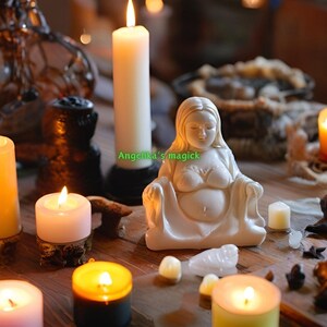 K&ouml;nnte beinhalten: Eine wei&szlig;e Keramikfigur einer schwangeren Frau, die mit ihren H&auml;nden auf ihrem Bauch sitzt. Die Figur ist umgeben von brennenden Kerzen, Kristallen und anderen spirituellen Gegenst&auml;nden. Der Text "Angela's magick" ist auf dem Bild zu sehen.