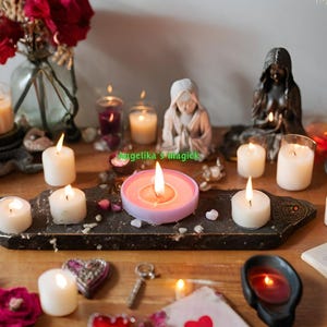 K&ouml;nnte beinhalten: Ein Tisch mit einer Auswahl an wei&szlig;en Kerzen, einer rosa Kerze und einem rosa Kerzenhalter. Auf dem Tisch stehen auch Blumen, ein Buch und andere Dekorationsartikel.