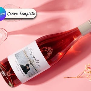 May include: A pink wine bottle with a white label that says "Congratulations, You're Engaged!" and features a photo of a couple on a beach. The bottle is on a pink surface.