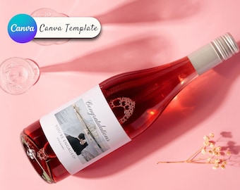 Puede incluir: Una botella de vino rosado con una etiqueta blanca que dice "¡Felicidades, estáis comprometidos!" y que presenta una foto de una pareja en una playa. La botella está sobre una superficie rosa.