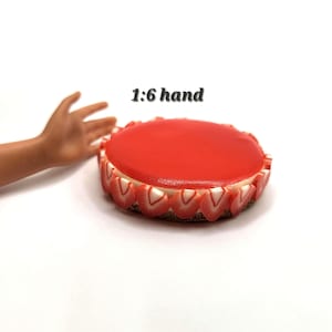 May include: A round dessert with a glossy red topping and a border of strawberry slices. The cake sits on a brown base and has a white cream filling. The text "1:6 hand" is visible.