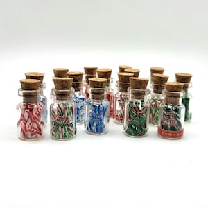 May include: A collection of small glass bottles with cork stoppers, filled with colorful candies and festive designs. Some bottles feature candy cane stripes, while others display Christmas-themed graphics and the text "Merry Christmas".