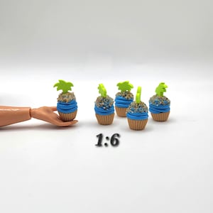 May include: Miniature cupcakes with blue frosting, tan cupcake liners, and green palm tree toppers. The cupcakes are arranged on a white surface. The text "1:6" is below the cupcakes.