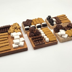 May include: A collection of miniature s'mores ingredients arranged on small wooden boards. The boards display graham crackers, chocolate bars, marshmallows, and cookies, perfect for a themed party or display.