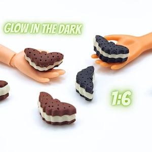 May include: Miniature ice cream sandwiches in a 1:6 scale, with a brown cookie exterior and white filling. The image includes the text "GLOW IN THE DARK" and "1:6".