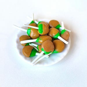 May include: A white plate with a pile of brown and green candy lollipops. The lollipops have a green swirl on the top and a white stick.