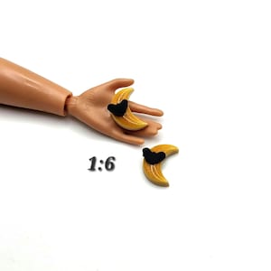 May include: Two miniature yellow crescent moon charms with black heart accents. The charms are on a white background. The number "1:6" is printed in black below the charms.