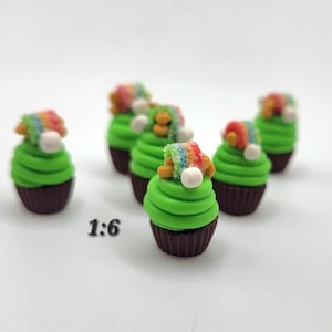 May include: Miniature cupcakes with green frosting and rainbow-colored decorations. Each cupcake has a brown base and a white ball on top. The text "1:6" is visible in the image.