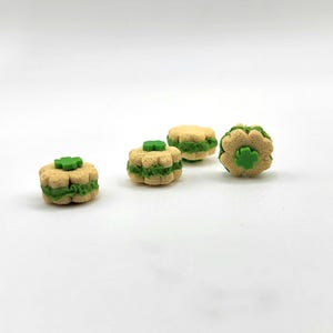 May include: Four small, decorative, shamrock-shaped objects. Each has a light tan exterior with a green filling and a green shamrock on top. The objects are arranged on a white background.