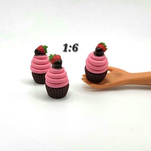 May include: Three miniature cupcakes with pink frosting and chocolate bases. Each cupcake is topped with a chocolate-covered strawberry. The text "1:6" is visible in the image.