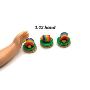 May include: Three miniature dollhouse food items. Each has a green base, a rainbow-colored cylinder, and a yellow top. The text "1:12 hand" is above the items. The items are on a white background.