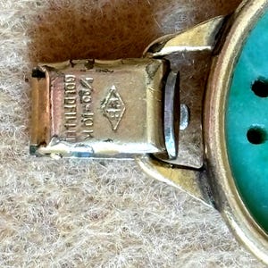 May include: Close-up of a gold-toned bracelet clasp with the text "1/20 10K Gold Filled" and a diamond-shaped hallmark. The bracelet features a turquoise-colored stone.