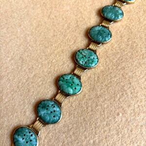 May include: A vintage bracelet featuring oval, carved jade stones in a vibrant green hue. The jade stones are set in a gold-toned metal frame and connected by gold links. The bracelet is displayed on a neutral-toned surface.